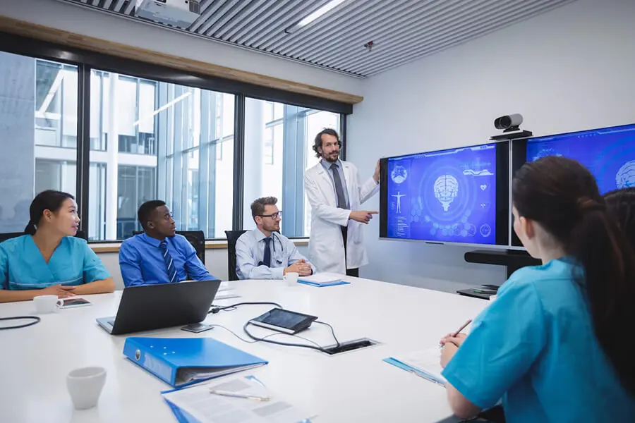 Medical team collaborating on healthcare data interoperability, with one professional presenting information on a large screen, illustrating connected systems and teamwork in healthcare technology.