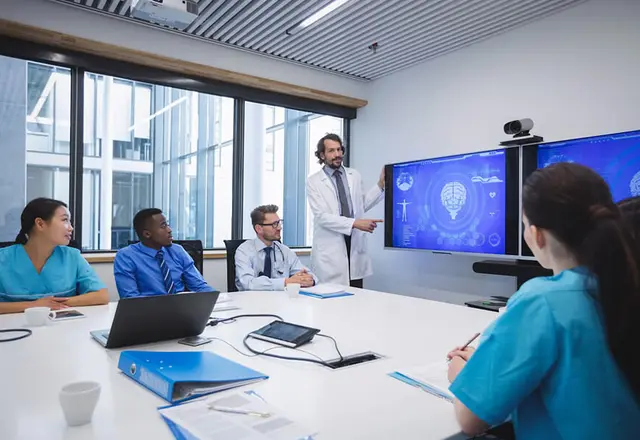Medical team collaborating on healthcare data interoperability, with one professional presenting information on a large screen, illustrating connected systems and teamwork in healthcare technology.
